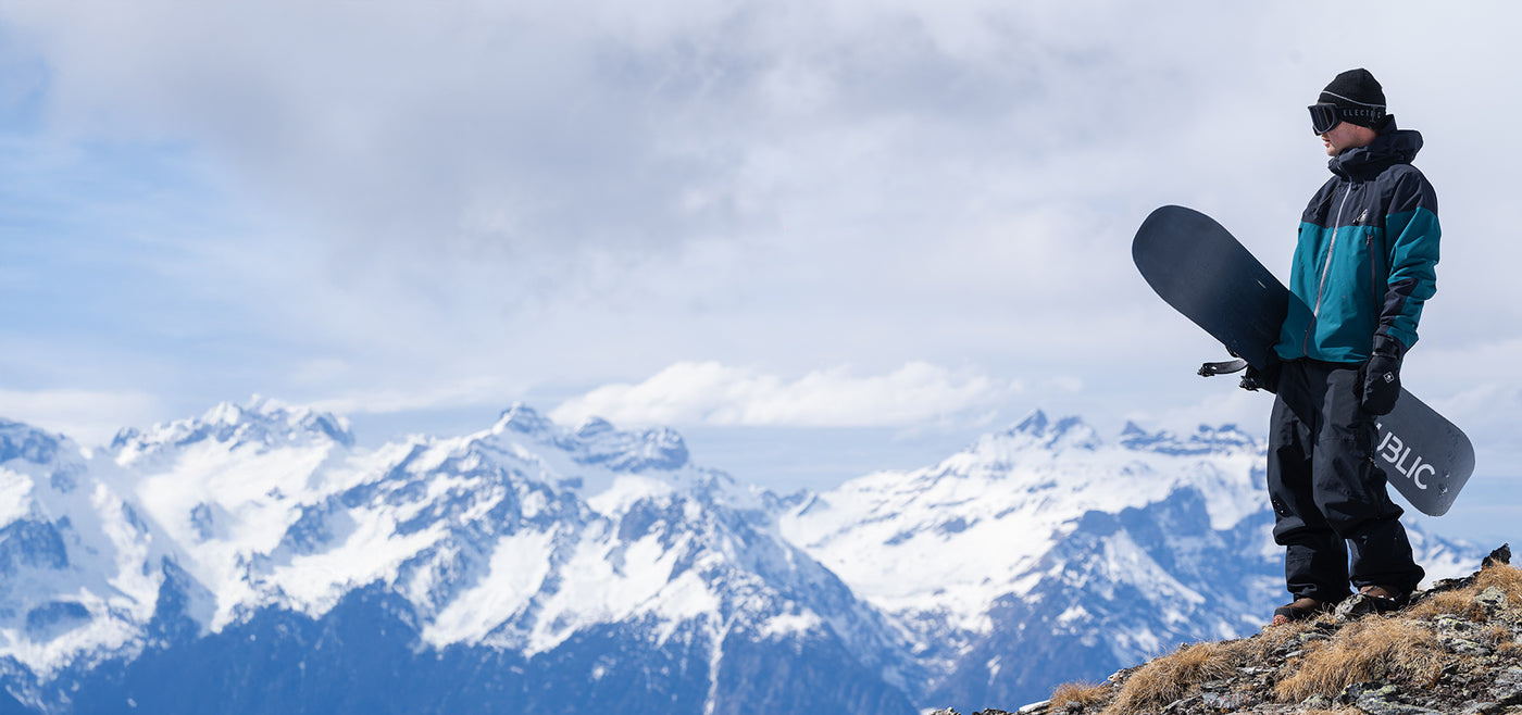 Man in gear and holding a snowboard on top of a mountain