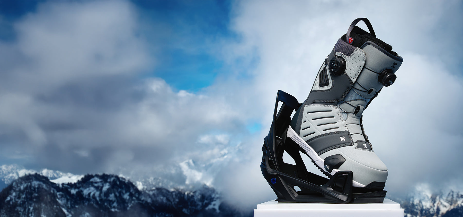 Snowboard boot on a snowy mountain peak with clouds in the background