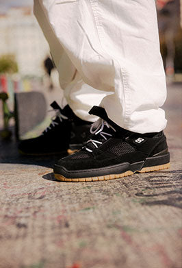 Black sneakers with white pants on a textured pavement