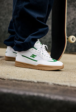 White sneakers with green accents worn by a person on a skateboard ramp.
