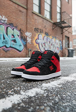 Black and red high-top DC sneakers on a street with graffiti in the background