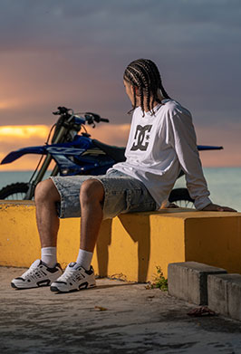 Person sitting on a yellow wall with a sunset and motorcycle in the background