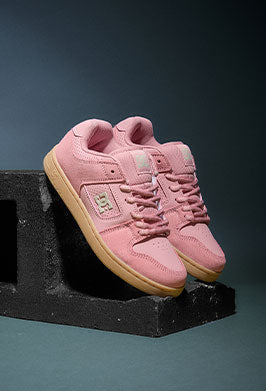 Pink sneakers with tan soles on a black stand against a dark background