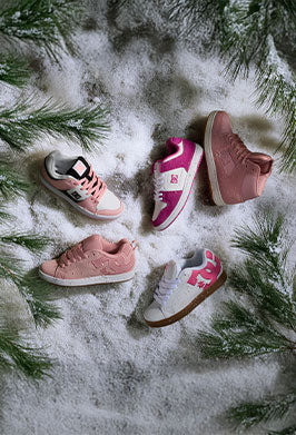 Five pairs of pink women's sneakers on a snowy surface with pine branches.