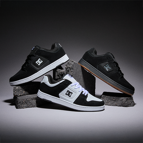 Three DC sneakers in black and white colorways displayed on dark textured blocks against a dark gray studio background.