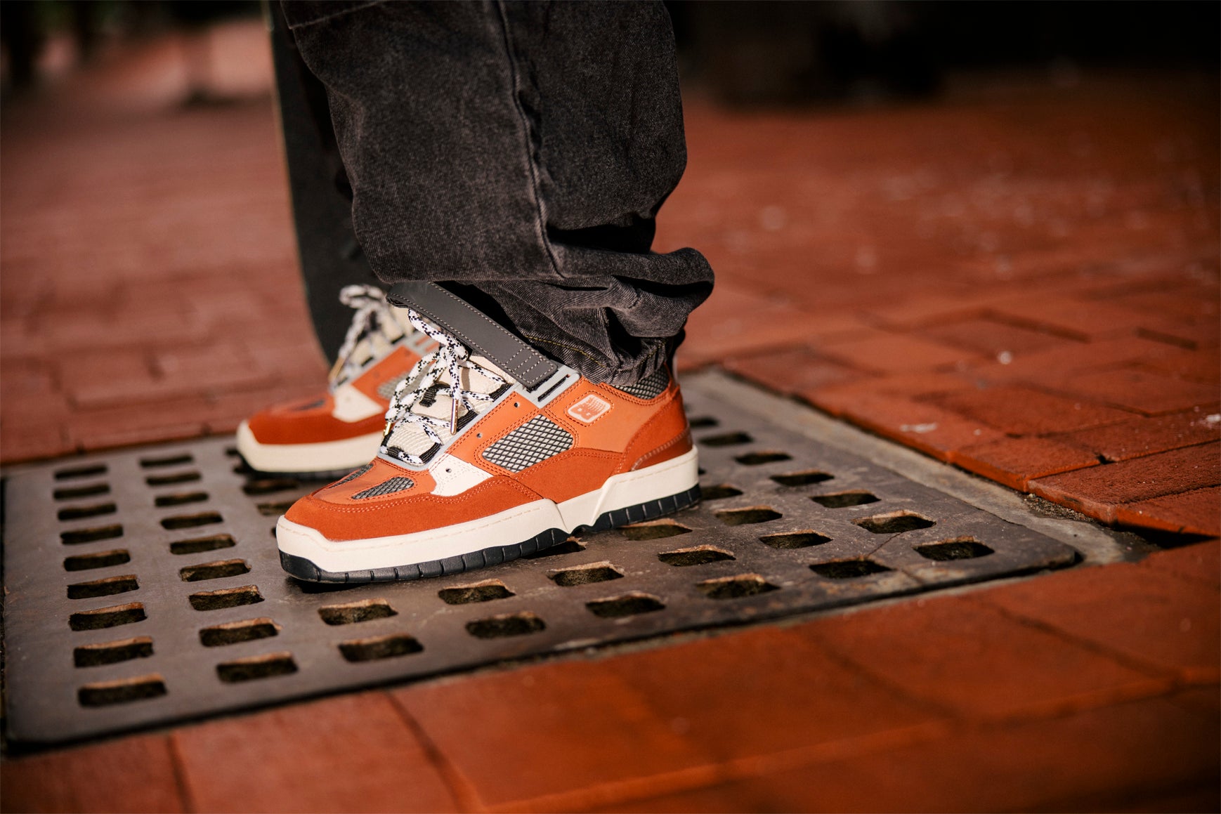 Person wearing orange sneakers stepping onto a metal grate on a brick surface