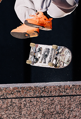 Person wearing orange sneakers and gray pants performing a trick on a skateboard with a black background
