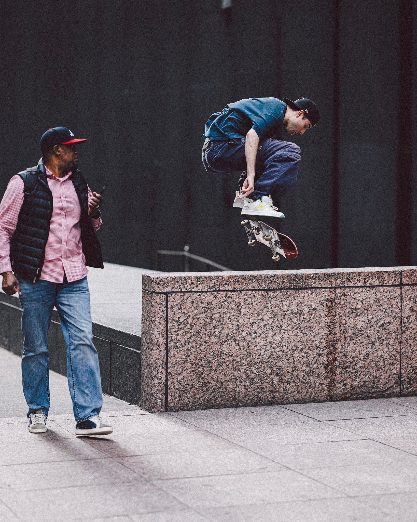 Person skateboarding mid-air with another person watching on a city street.