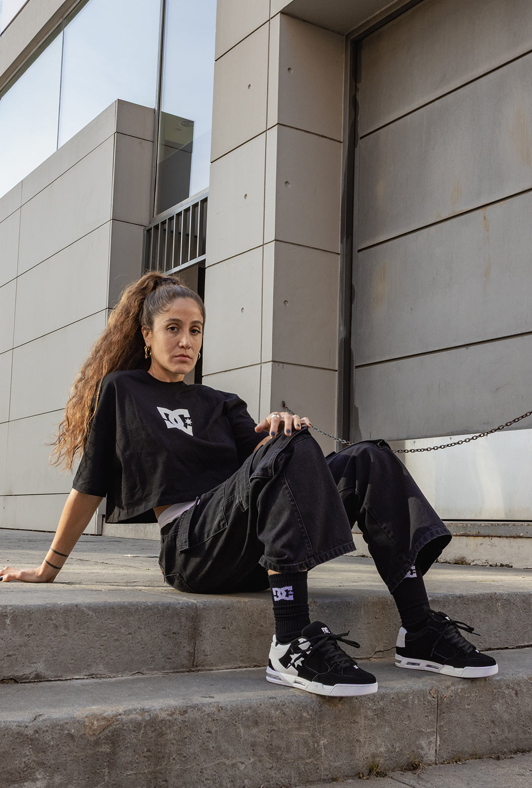 Woman sitting on steps wearing a black outfit with visible branding.