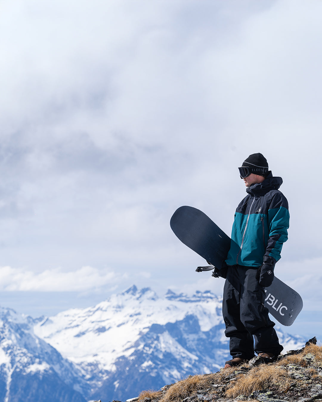 Person holding a snowboard with mountains in the background