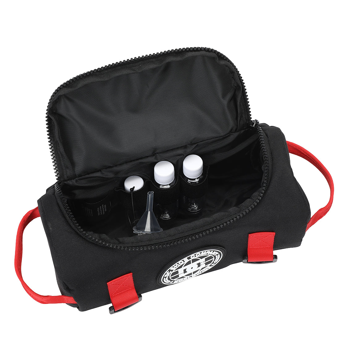The DC Shoes DC Runner Dopp Kit is a black zippered bag with red handles and a round white logo. Inside, it contains small bottles with white caps, a funnel, and a dropper.