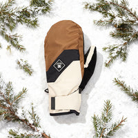 Brown, beige, and black winter glove on a snowy background with pine branches.