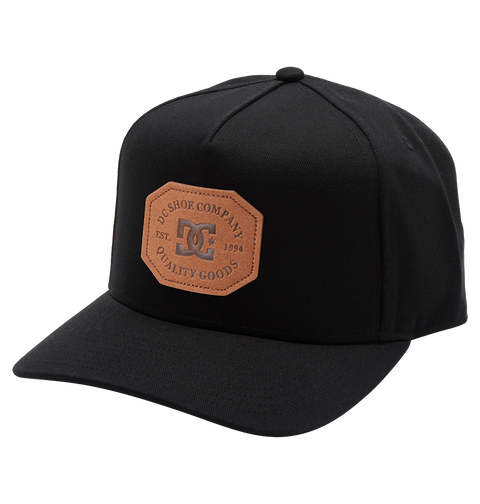 The Men's Reynotts Cap by DC Shoes is a black skate cap with a curved brim, featuring a brown leather front patch debossed with “DC Shoe Company, Est. 1994, Quality Goods.”.