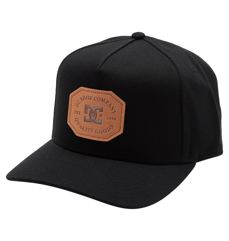 The Men's Reynotts Cap by DC Shoes is a black skate cap with a curved brim, featuring a brown leather front patch debossed with “DC Shoe Company, Est. 1994, Quality Goods.”.