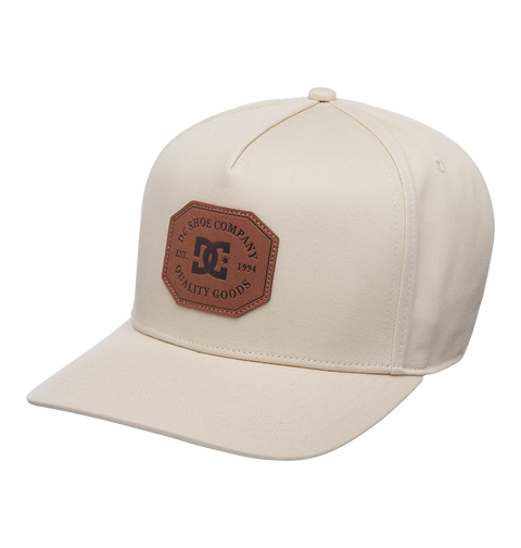 The Men's Reynotts Cap by DC Shoes is a beige six-panel skate cap with a curved brim and a brown leather patch on the front featuring the DC logo.