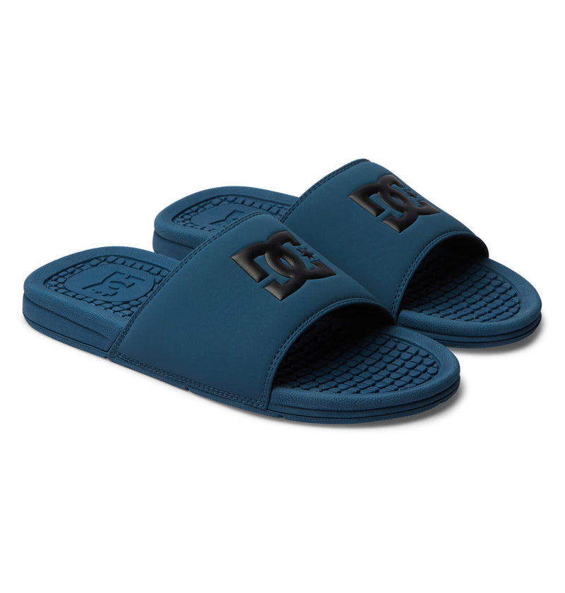 The Men's Bolsa Slides from DC Shoes feature blue wide straps with a raised black DC logo and textured footbeds, offering a sporty, casual style perfect for relaxing after skating.