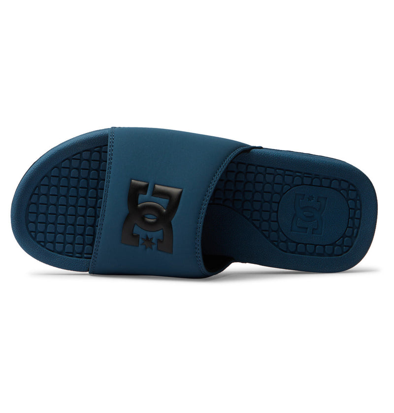 The DC Shoes Men's Bolsa Slides feature a dark blue wide strap with a raised black DC Shoes logo, paired with a textured black sole. Seen from the side, they offer comfort and style—ideal for relaxing after skating.