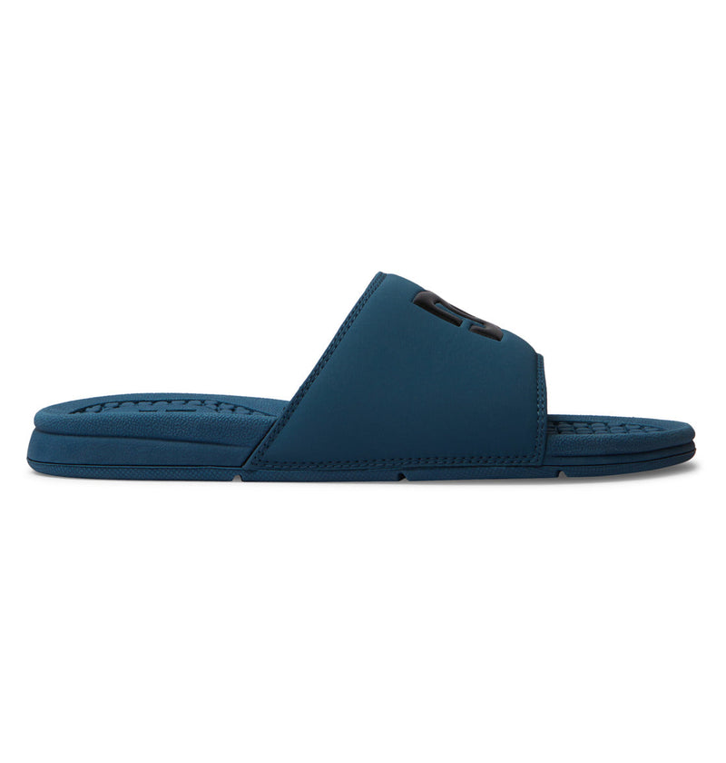 The DC Shoes Men's Bolsa Slides in blue feature a thick strap with raised logo, textured footbed, and flat sole—ideal for post-skate relaxation. Shown in side profile against a white background.