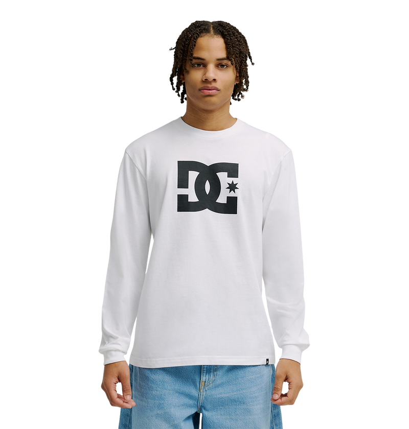 A person in the Men's DC Star Tee by DC Shoes—white with bold black DC graphics—stands against a plain white background, paired with light blue jeans. Ideal for casual hangouts or skate sessions.