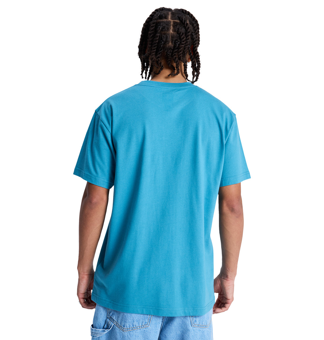 A person with braided hair faces away from the camera, wearing a blue DC Star Hss t-shirt by Reebok and light blue denim shorts against a white background.