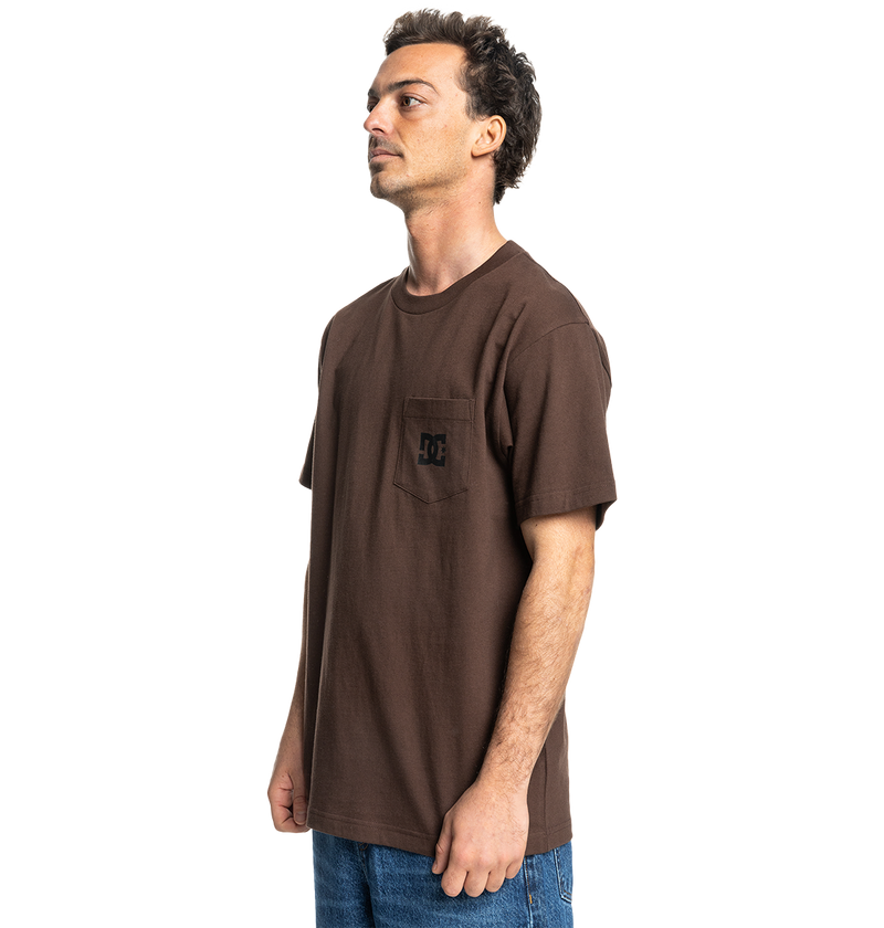 A man stands sideways against a white background, wearing the Men's DC Star Pocket Tee by DC Shoes—a relaxed fit brown skate shirt with a chest pocket and small logo—paired with blue jeans.