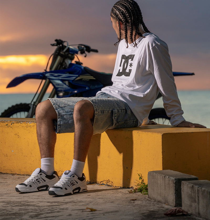 Person sitting on a yellow wall with a motorcycle in the background during sunset wearing the AT-2 shoes