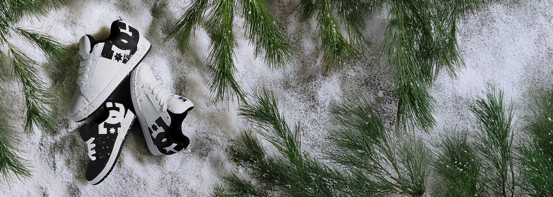 Black and white Court Graffik sneakers on a snowy ground with pine branches
