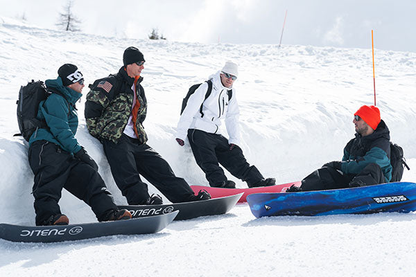 Four people sitting on snowboards in a snowy landscape