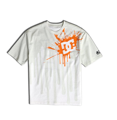 White T-shirt featuring an orange paint splatter with a bold DC logo on the upper left chest, and subtle light gray drips across the front. There is a small black 43 on the left sleeve.