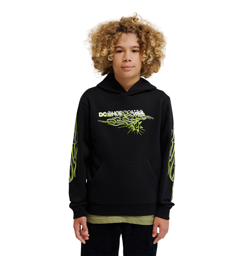 A young person with curly hair wears the DC Shoes Side Flame Hoodie Youth, a black pullover featuring neon green designs and a bold DC Shoes logo, standing against a plain white background.