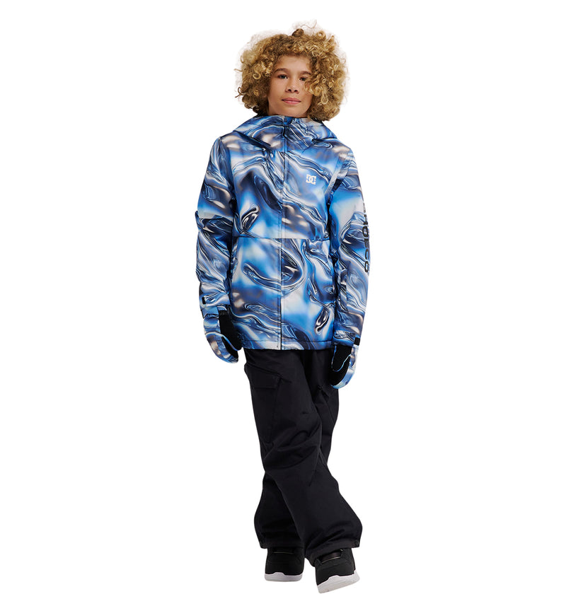 A young person with curly hair wears the DC Shoes Basis Youth Jacket, featuring a blue and black pattern, paired with black pants and black shoes, standing against a plain white background.