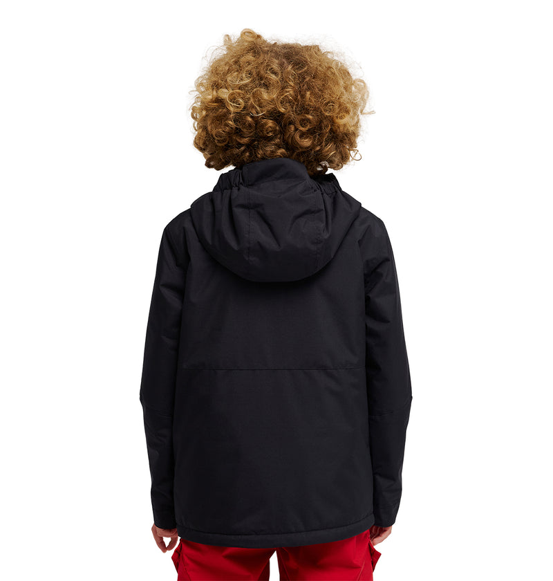 A person with curly hair is seen from behind, wearing the DC Shoes Basis Youth Jacket in black and red pants, standing against a white background.