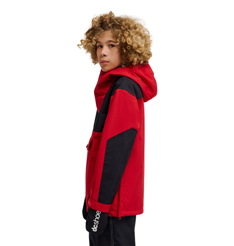 A young person with curly hair is standing sideways and looking over their shoulder, wearing the DC Shoes DC-43 Youth Anorak—a red and black hooded snow jacket featuring black accents on the sleeves and dcshoes branding at the wrist.
