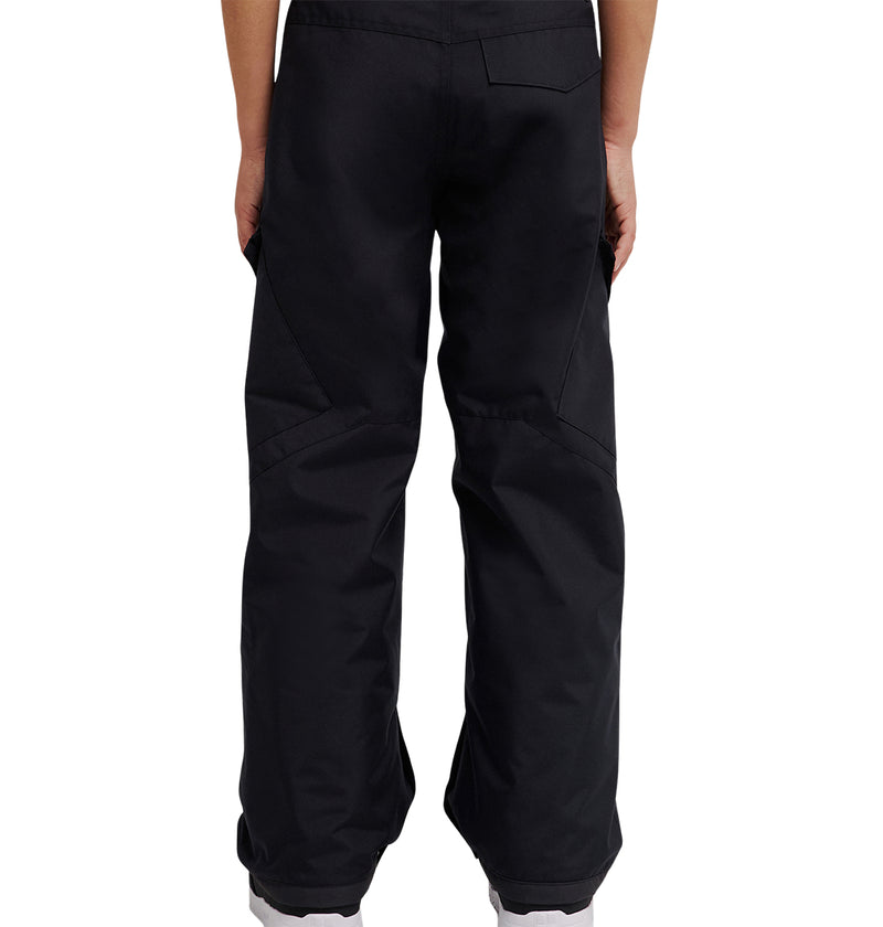 A person is shown from the back wearing DC Shoes’ Banshee Youth Pants—loose-fitting black pants with two back pockets and seam details reminiscent of classic youth snow gear. Only the lower torso and legs are visible, with white shoes peeking out at the hem, highlighting a design that emphasizes comfort and insulation.