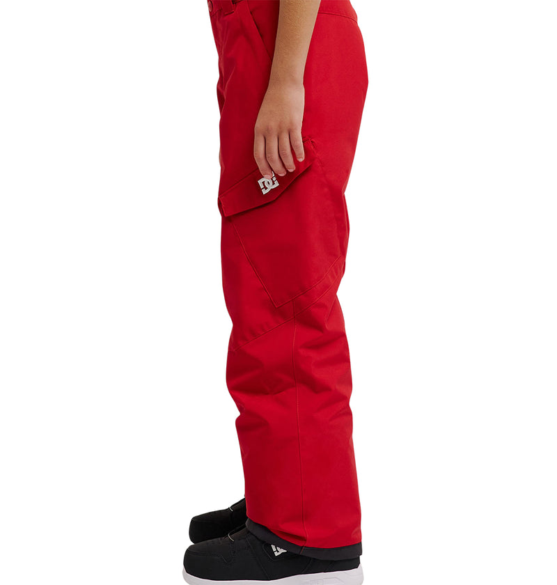 A person stands in profile wearing bright red DC Shoes Banshee Youth Pants and black sneakers against a white background.