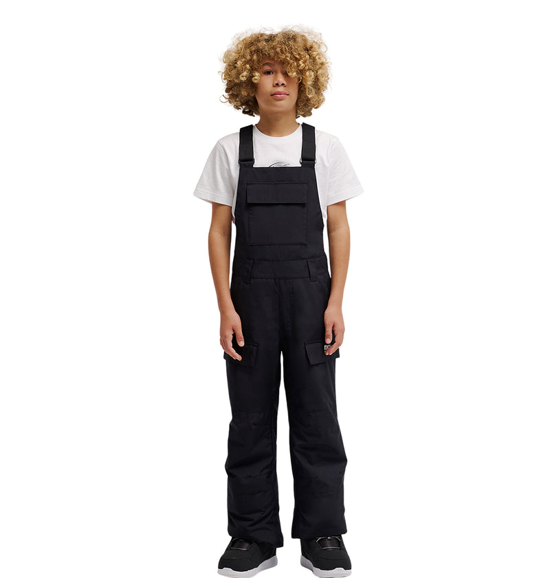 A person with curly blond hair wearing a white t-shirt under the DC Shoes Roadblock Youth Bib and black shoes stands facing forward against a plain white background.