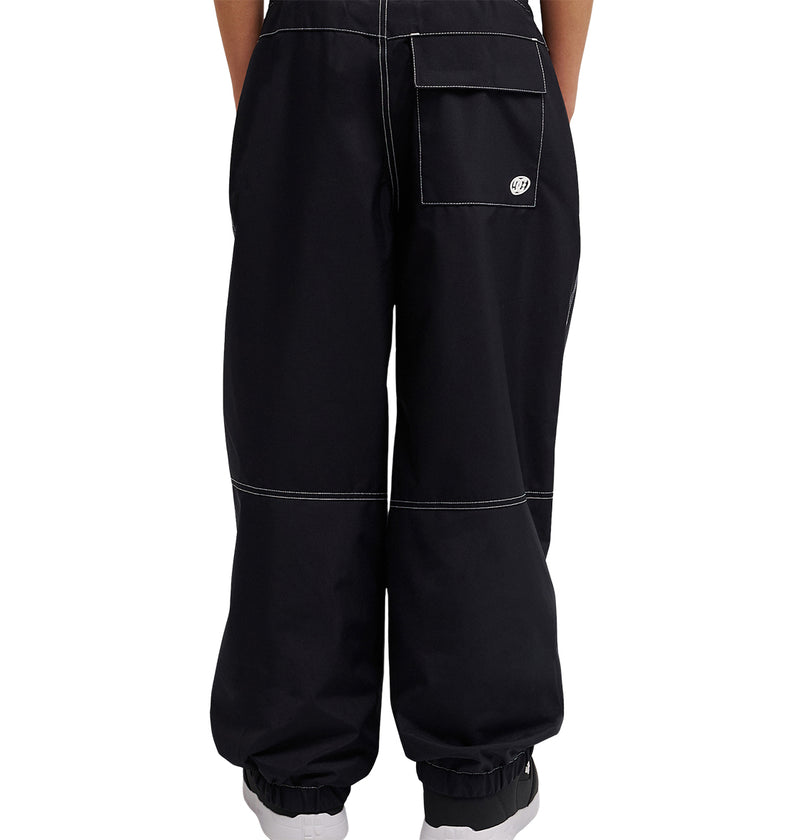 A person is shown from the waist down, wearing black DC Shoes Trackstar Baggy Youth Pants featuring white stitching, elastic cuffs, and a large back pocket. These cargo pants are designed for enhanced snow performance and are set against a white background.