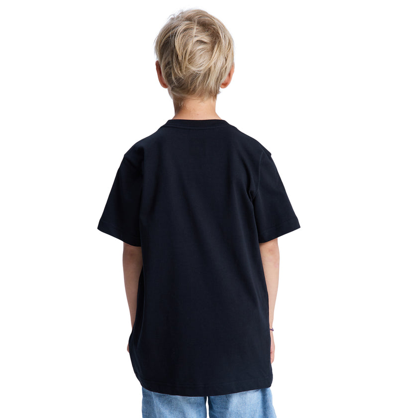 A young blond-haired child is seen from behind, wearing the Reebok DC Star Filled Ss Boy t-shirt and light blue jeans against a white background.