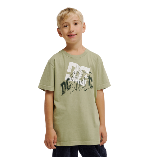 A young boy with short blond hair is wearing the DC Shoes DC Speratic Tee Youth, a relaxed fit light green graphic skate t-shirt featuring heritage-inspired artwork, along with dark pants, as he stands and smiles against a plain white background.