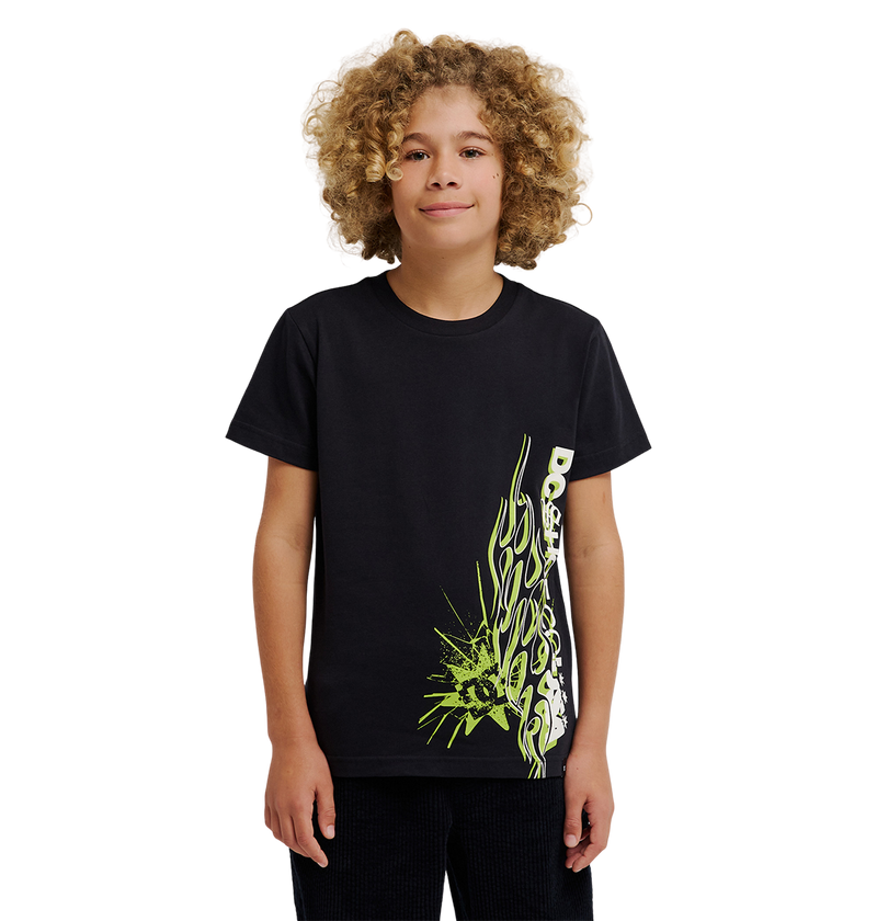 A young person with curly blond hair wears the DC Shoes DC Side Flame Tee Youth, a relaxed fit black skate t-shirt featuring a neon green and white abstract design on the lower side, standing against a plain white background.