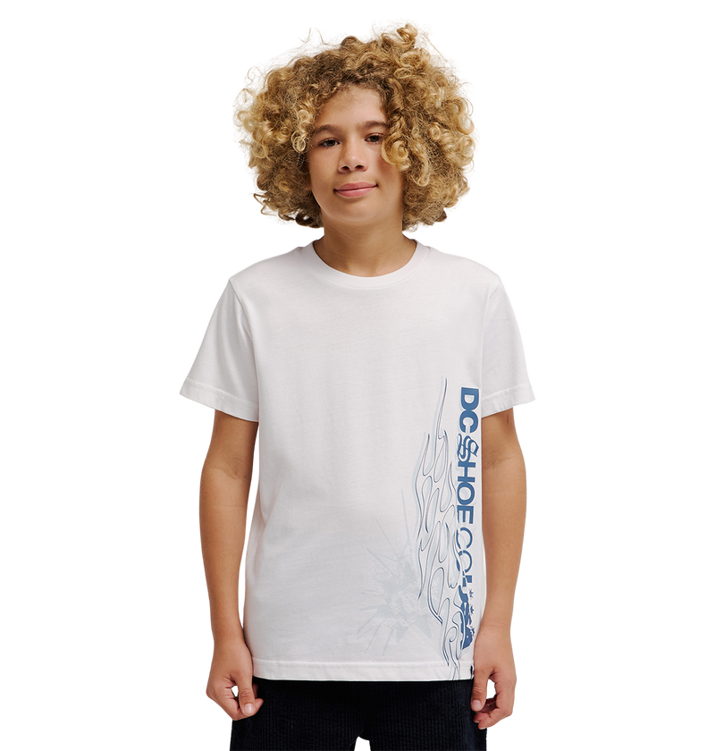 A child with curly blond hair poses against a plain white background, wearing the DC Shoes Side Flame Tee Youth—a relaxed fit white T-shirt with blue "DC SHOE CO." text and an abstract flame artwork design on the lower side.