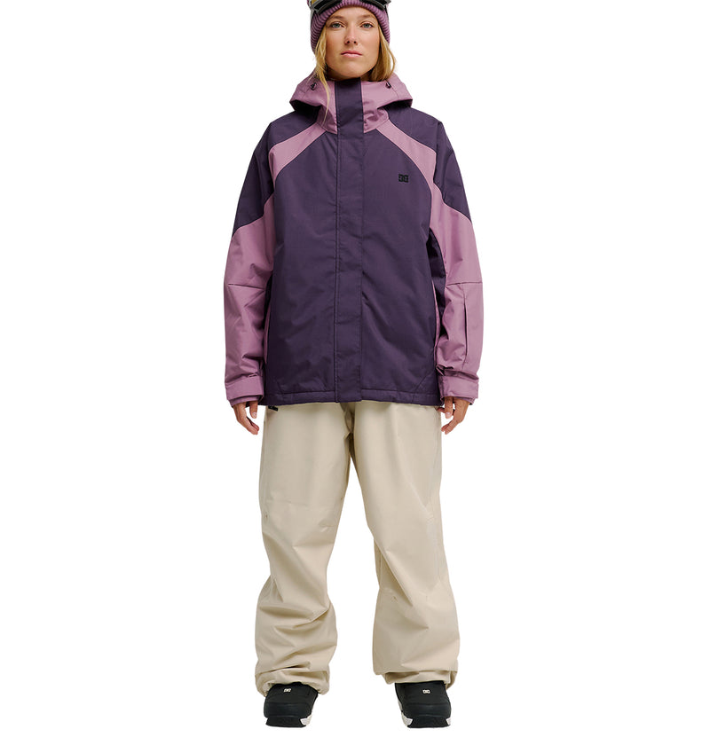 A person wearing the DC Shoes Everfrost Jacket—a purple and pink waterproof jacket—along with beige snow pants, black boots, and a purple hat stands facing forward against a white background, ready for peak snow performance.