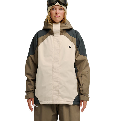 A person wearing the DC Shoes Everfrost Jacket in beige and olive-green, featuring insulation and a hood, along with ski goggles, stands facing forward against a white background.
