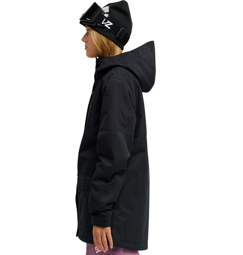 A person wearing a black hooded waterproof Cruiser Jacket from DC Shoes, a black beanie, and ski goggles stands in profile facing left. They are also dressed in purple pants against a white background.