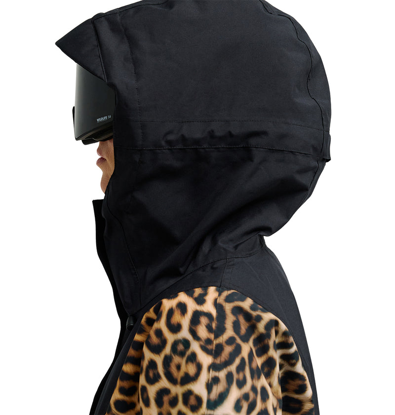 A person wearing the DC Shoes Chalet Anorak—a black hooded jacket with leopard print sleeves designed for breathability and reliable waterproofing—poses in profile against a white background, accessorized with large black sunglasses.
