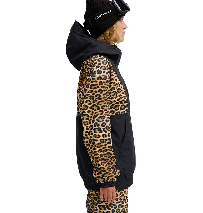 A person in profile view wears the DC Shoes Chalet Anorak, a jacket with leopard print sleeves and hood paired with matching pants. The insulated anorak features a solid black section across the chest and lower body, combining standout style with elevated snow performance. A black beanie and ski goggles complete the look.