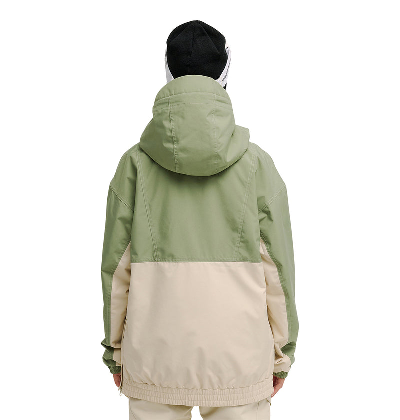 A person faces away, wearing the DC Shoes Chalet Anorak in two-tone light green and beige with matching pants. The hood is up, and they sport a black and white beanie. Engineered with advanced snow performance and waterproofing, the outfit stands out against the plain white background.