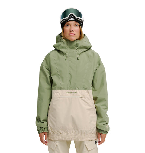 A person wearing the DC Shoes Chalet Anorak in green and beige, paired with beige pants and ski goggles, stands facing forward against a white background, ready for optimal snow performance.