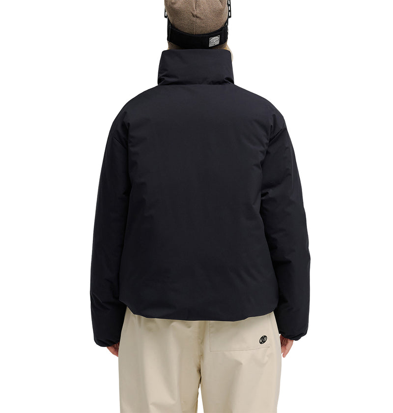 A person is facing away, wearing the DC Shoes Aura Puffer Jacket in black, paired with beige pants and a beige beanie. The plain white background highlights the outfit from the back.