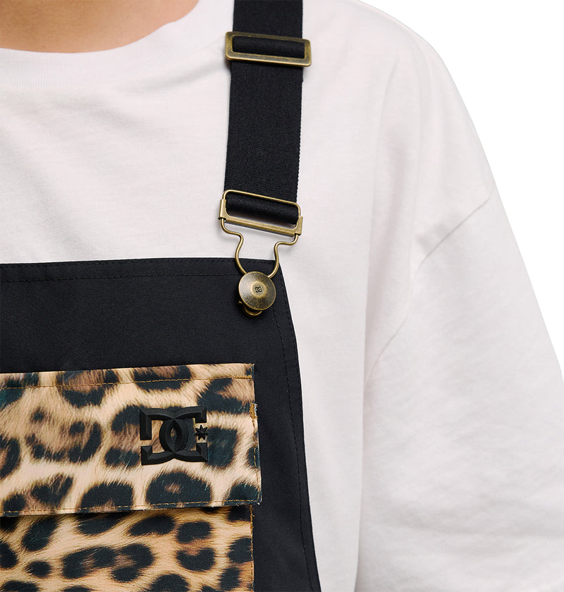 A person wears DC Shoes’ Valiant Bib Pants, featuring black overalls with a leopard print chest pocket displaying the DC logo and paired with a white shirt, offering breathable protection. Only the chest and strap area are visible against a white background.